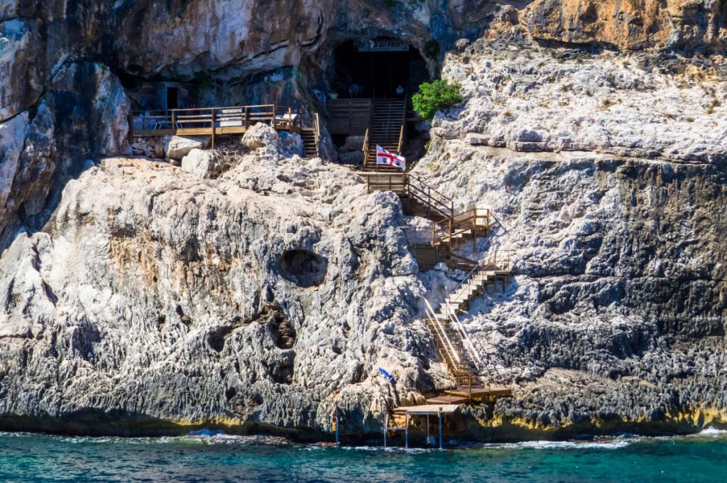 Scalinata verso una grotta sul mare con piattaforma di legno e bandiera.