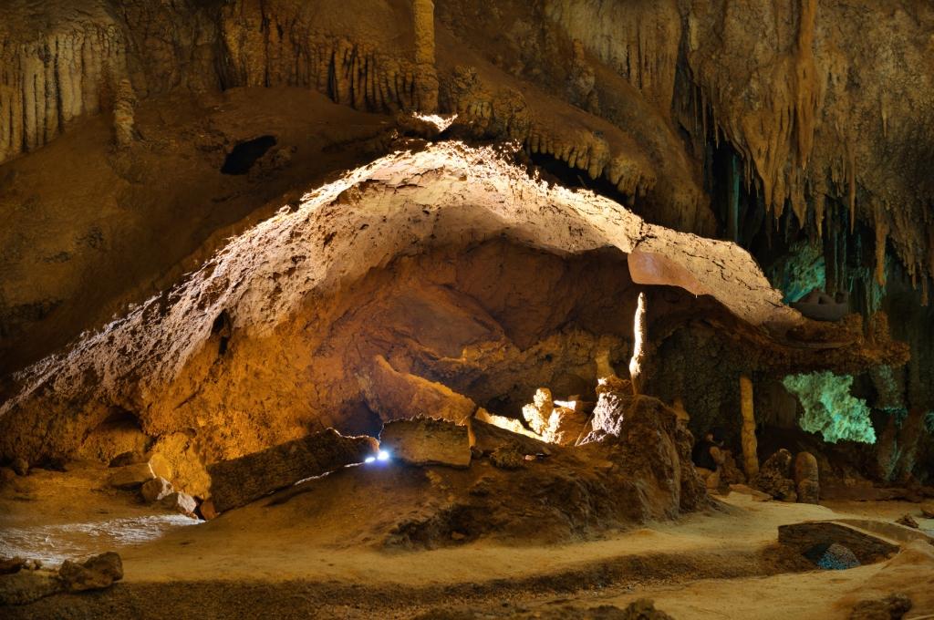 Interno di una grotta con stalattiti e stalagmiti illuminate da luce calda.