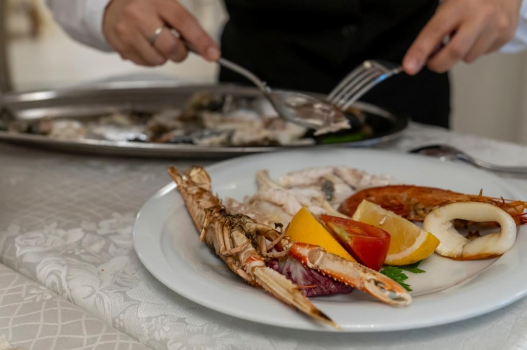 Piatto di pesce con crostacei, limone e pomodoro su tovaglia elegante.