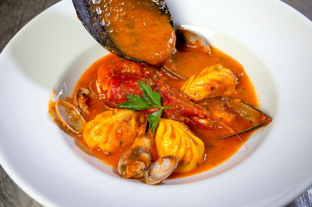Zuppa di pesce con ravioli, gamberi e vongole in salsa rossa.