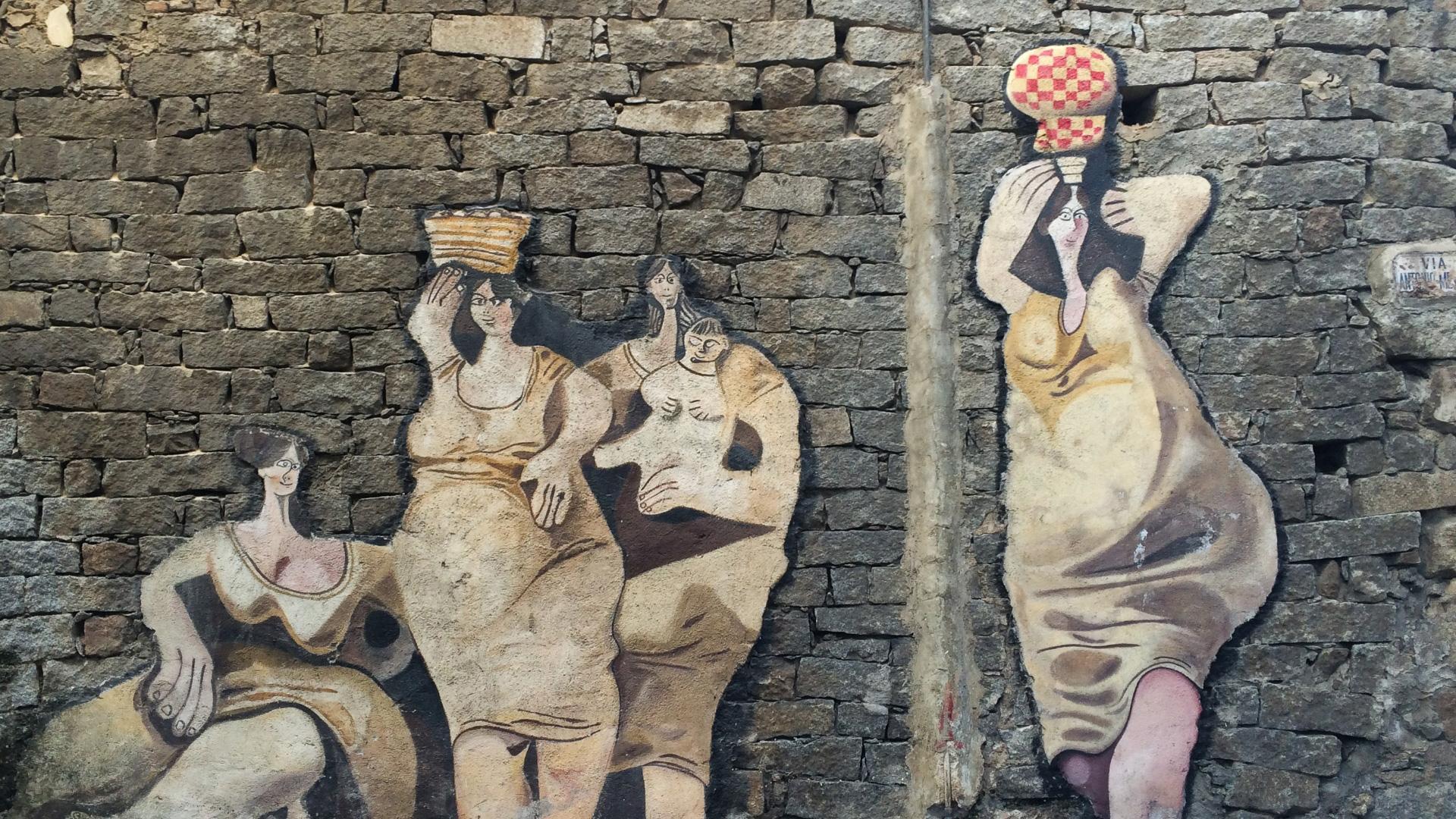 Mural of rural women on a stone wall, evoking strength and community.