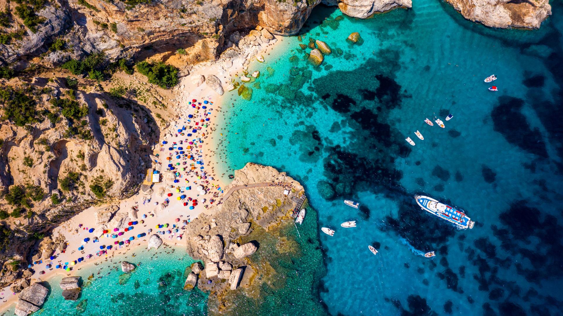 Crowded beach, crystal-clear sea, boats: a vibrant, colorful summer paradise.
