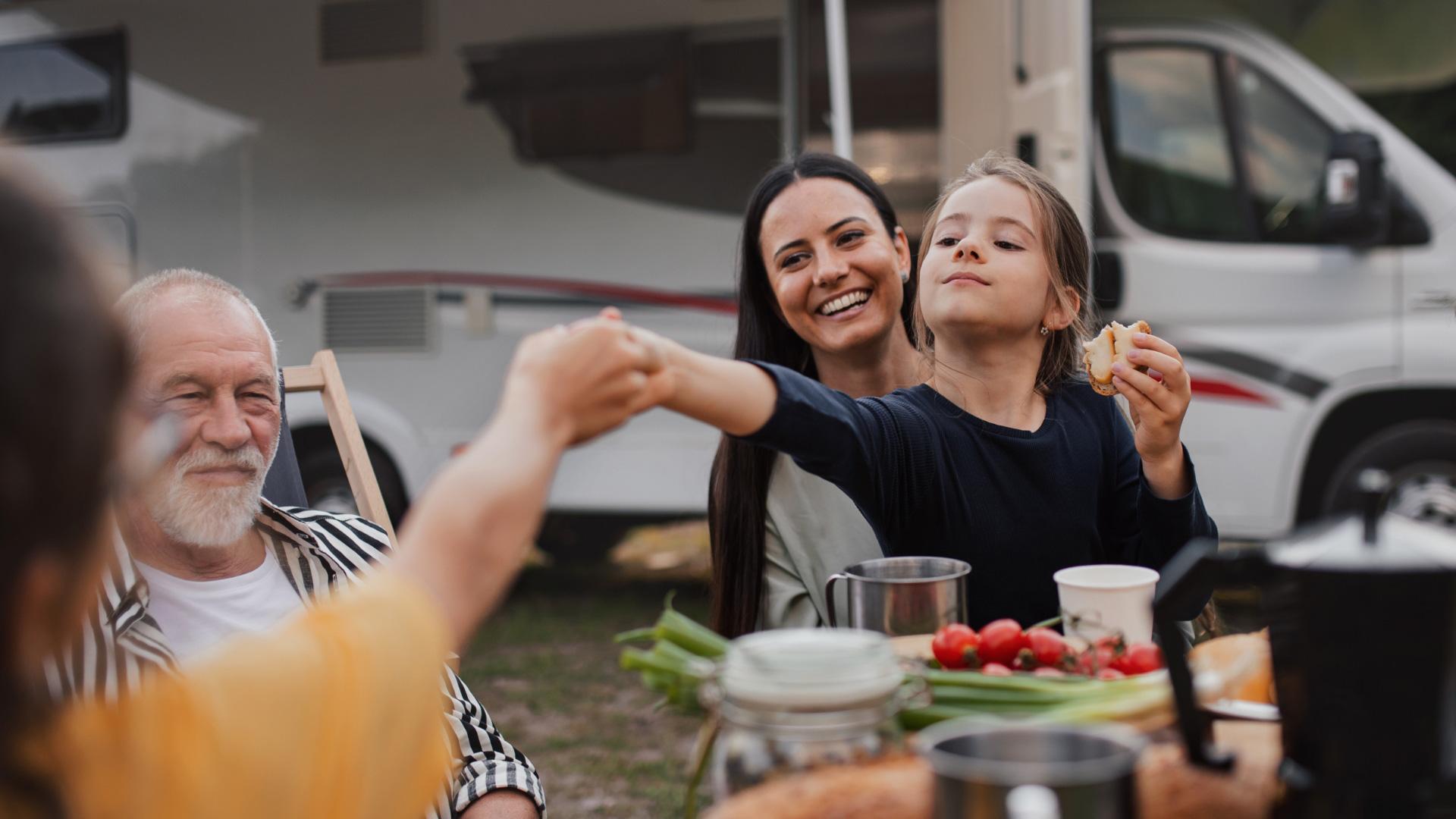 Famiglia felice in campeggio, sorrisi e condivisione di cibo all'aperto.
