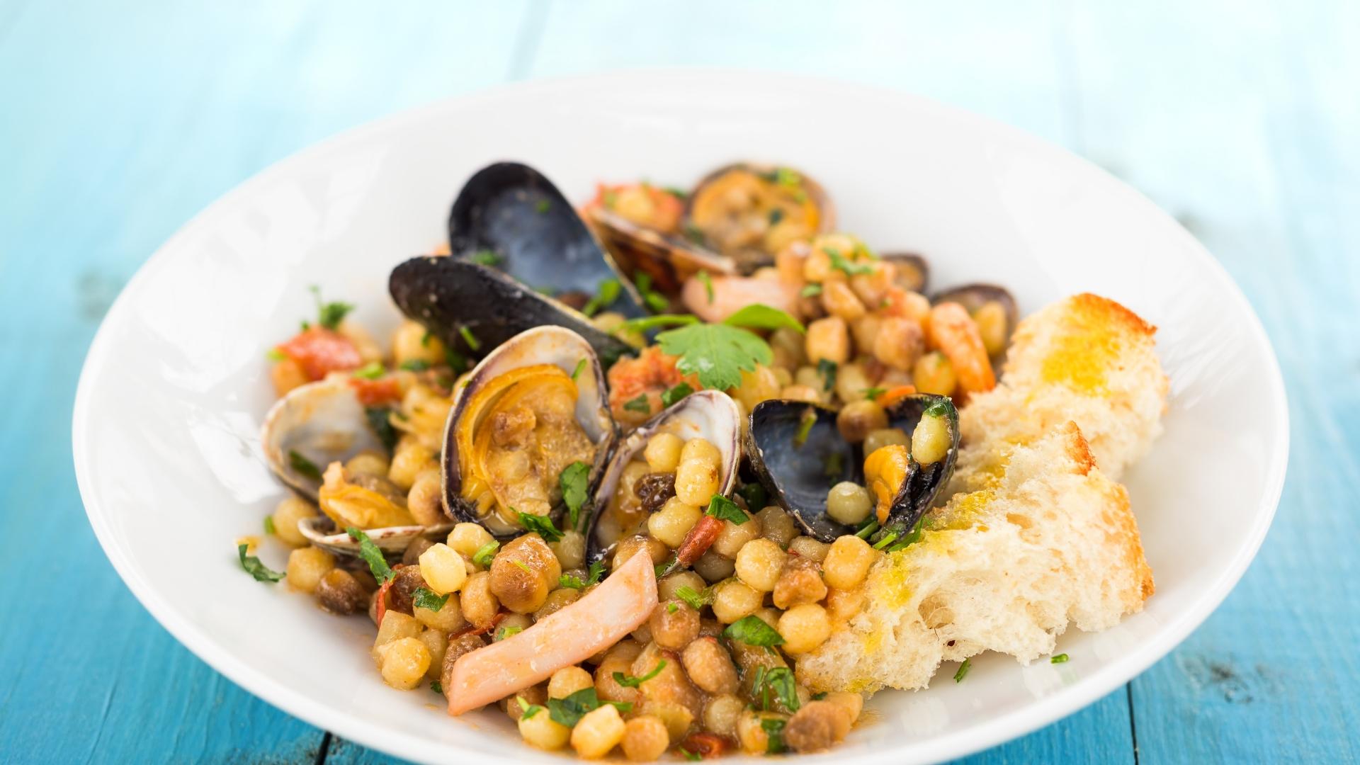 Piatto di fregola con frutti di mare e pane croccante, fresco e invitante.