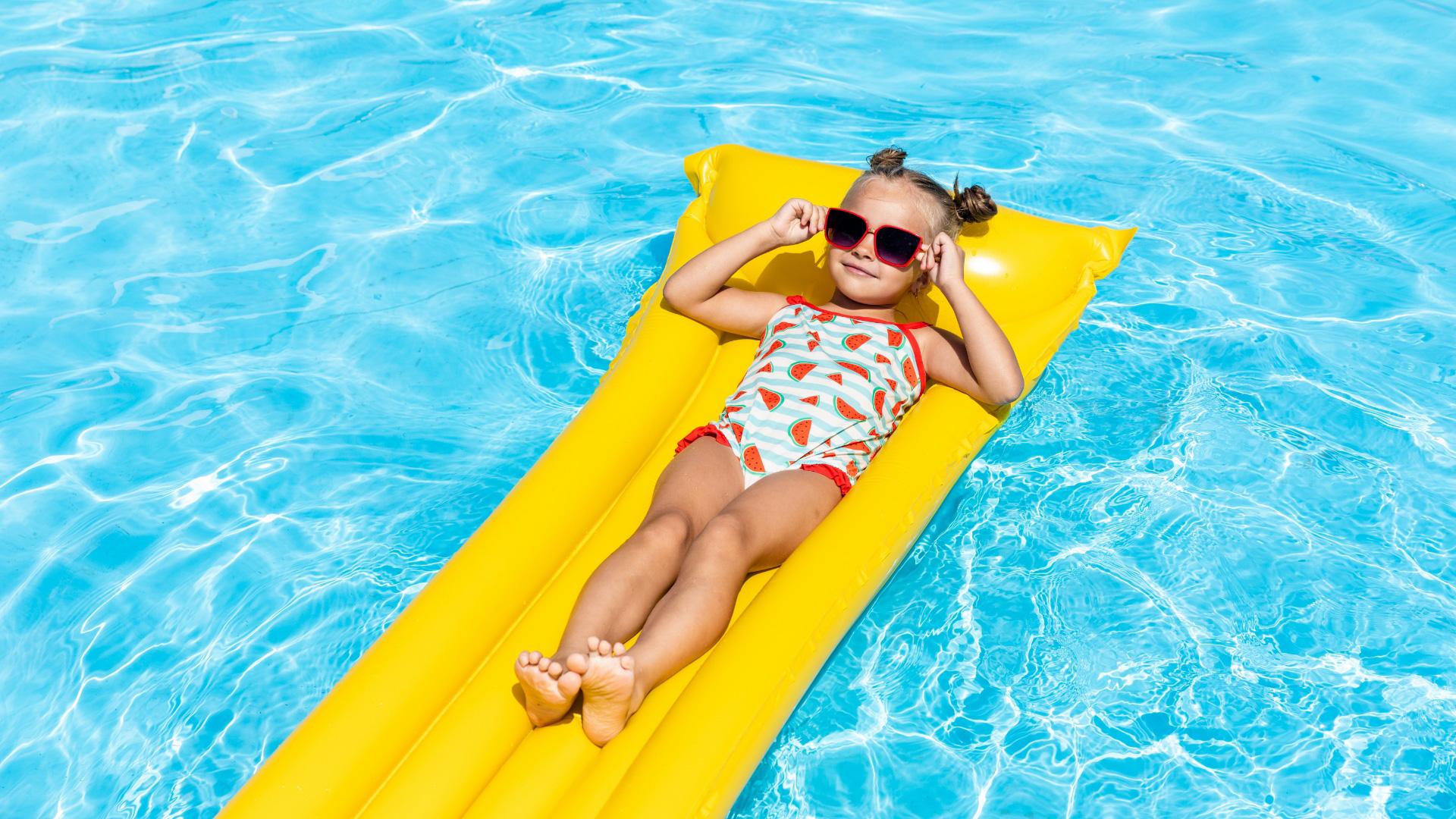 Happy child on yellow float in pool, enjoying summer sun and relaxation.