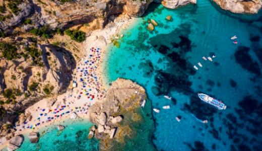 Spiaggia con acque turchesi, barche e ombrelloni colorati, circondata da scogliere.
