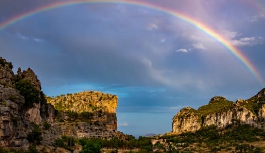 Arcobaleno sopra un paesaggio montano con cielo nuvoloso e formazioni rocciose.